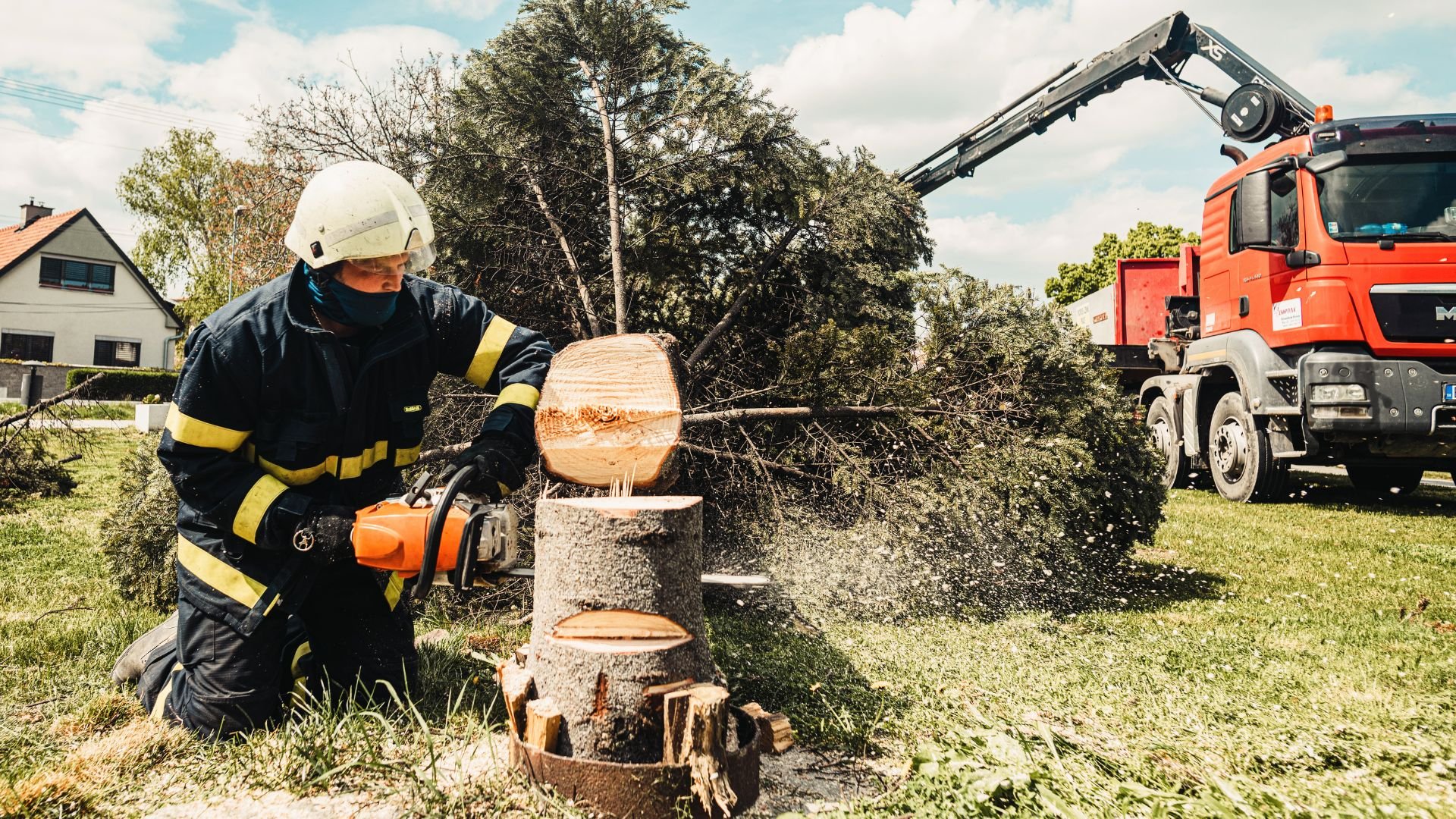 Firefighter cutting tree with chainsaw near red emergency truck