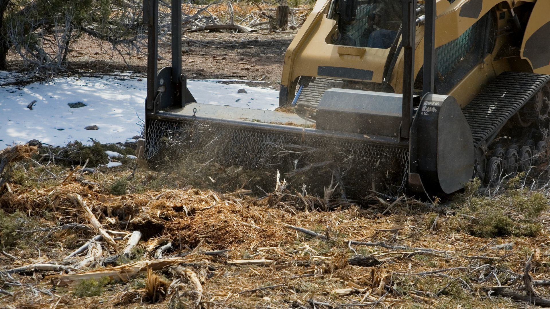Yellow bulldozer clearing snow and debris in winter forest landscape
