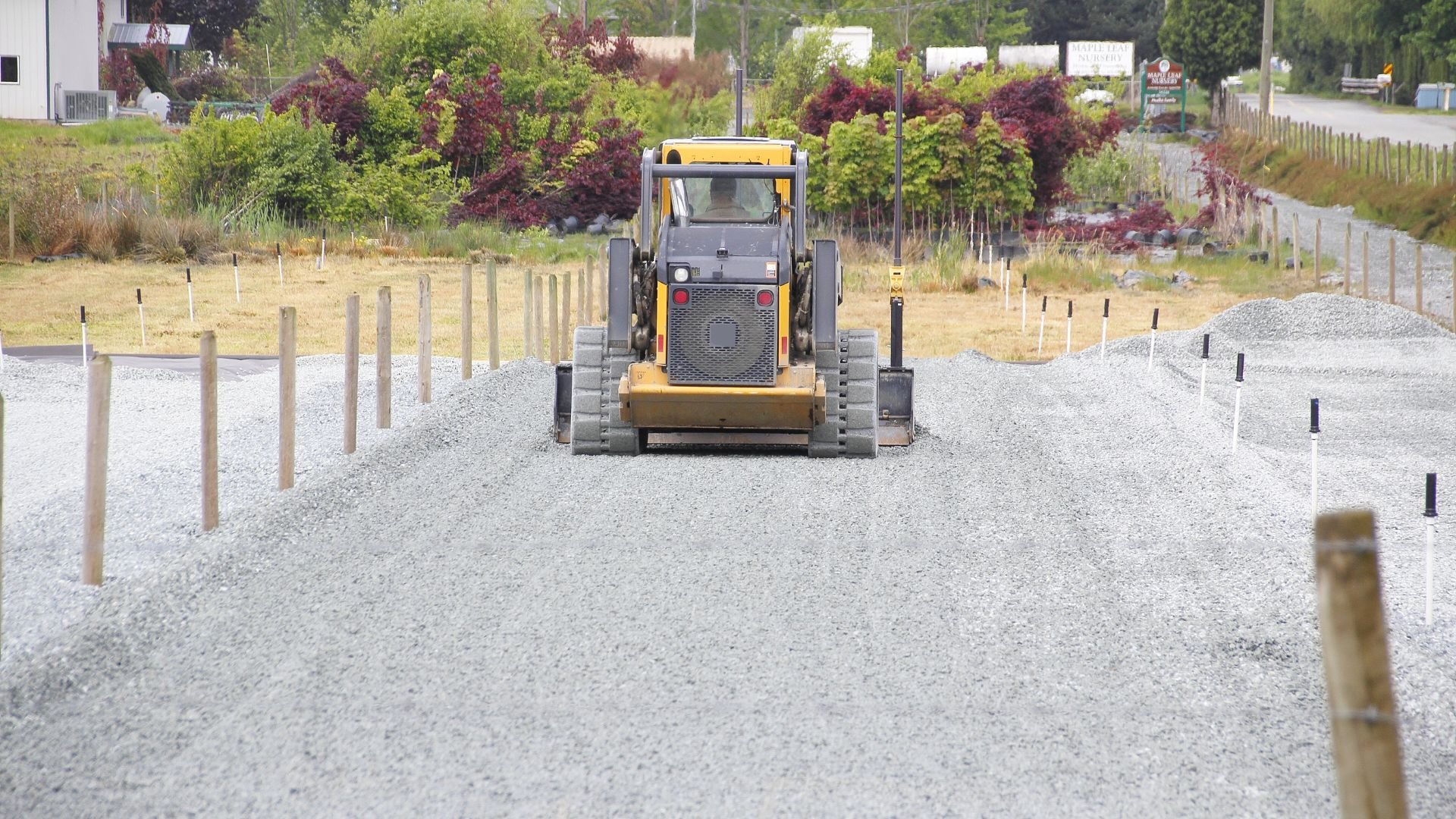 Yellow skid steer working on gravel road with wooden fence posts