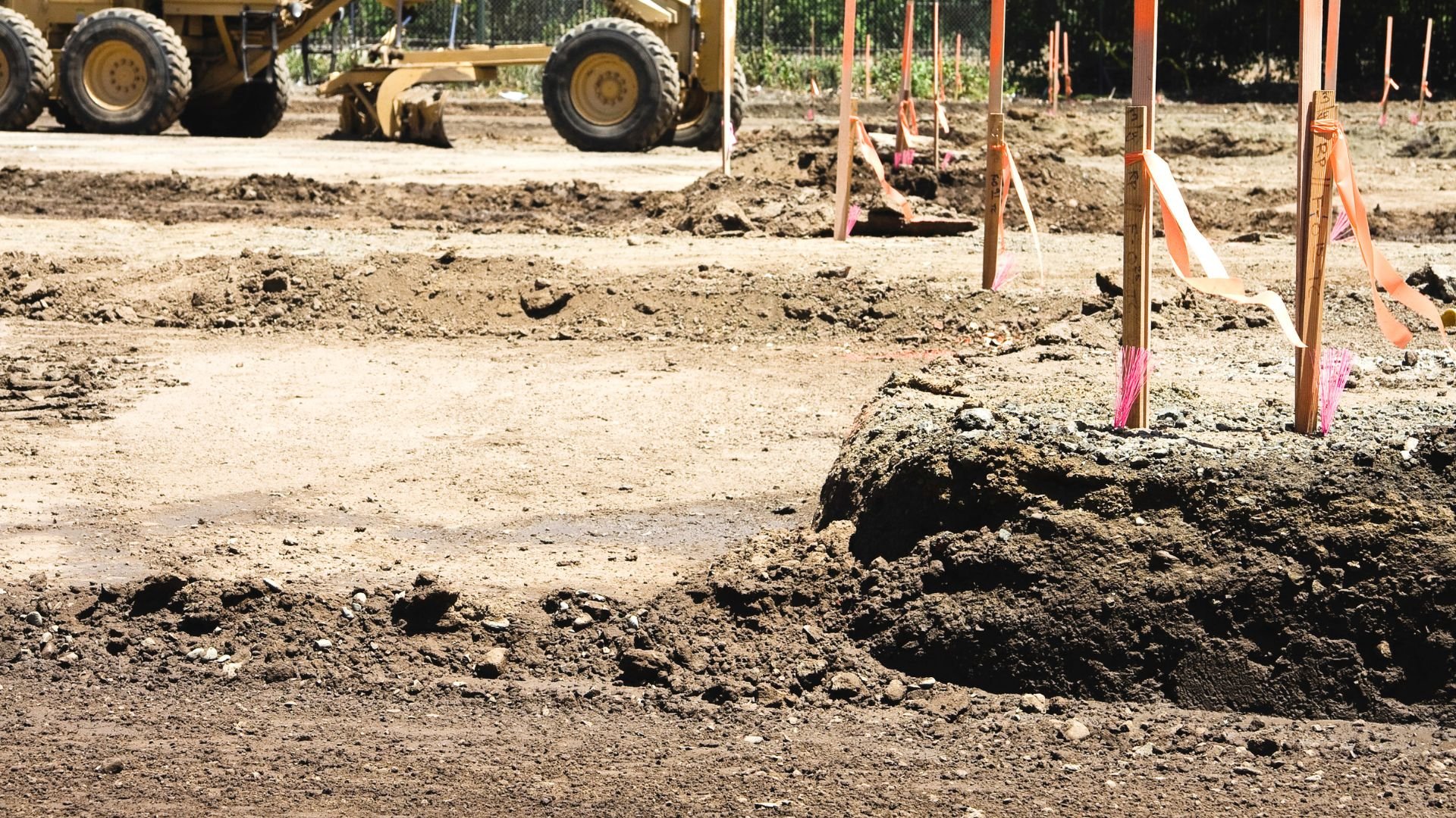 Construction site with grader and survey stakes on dirt ground