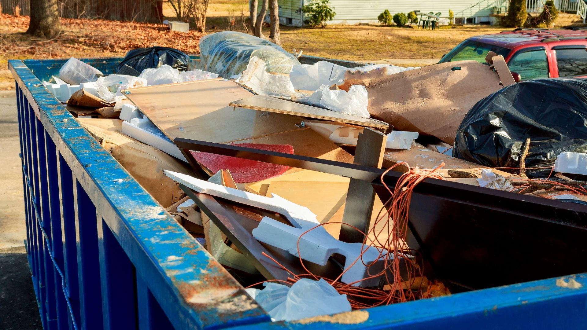 Blue dumpster filled with debris, construction waste, and garbage bags