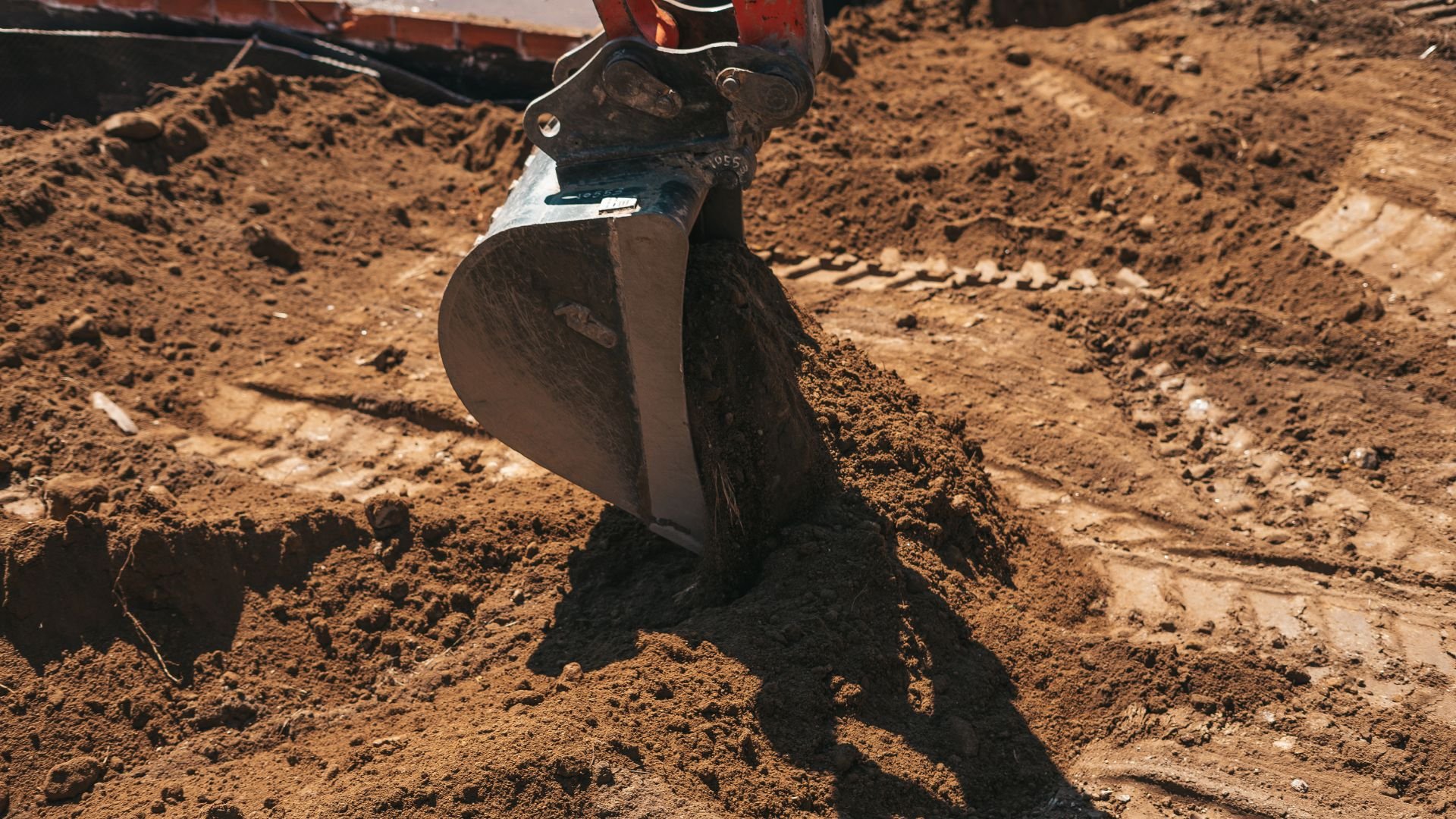Excavator bucket digging into brown soil at a construction or mining site